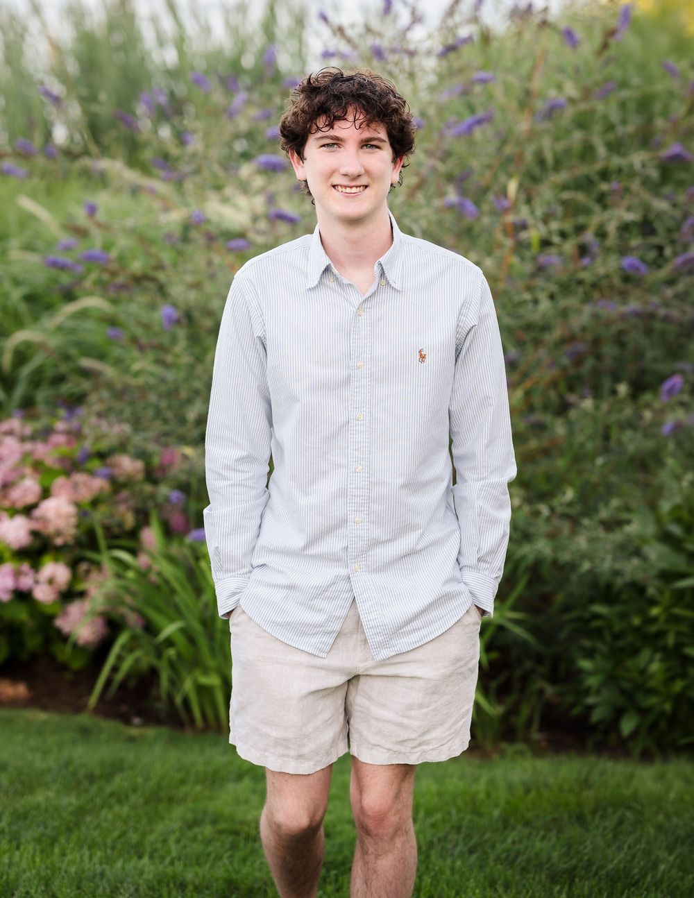 Young man in light blue Polo Ralph Lauren shirt and khaki shorts standing in a lush garden.