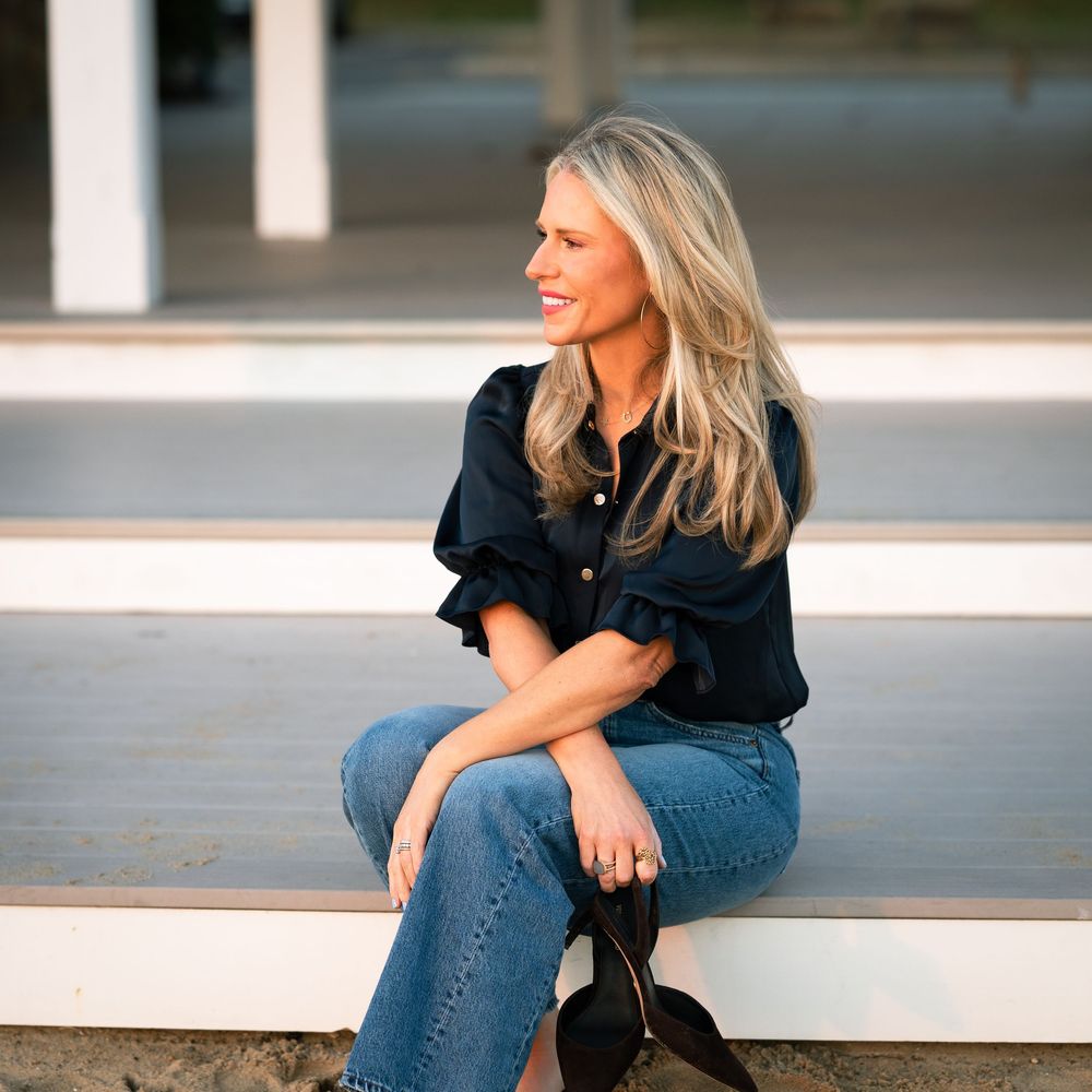 Woman in denim and black shirt sitting casually on concrete steps while looking to the side on a sunny day.