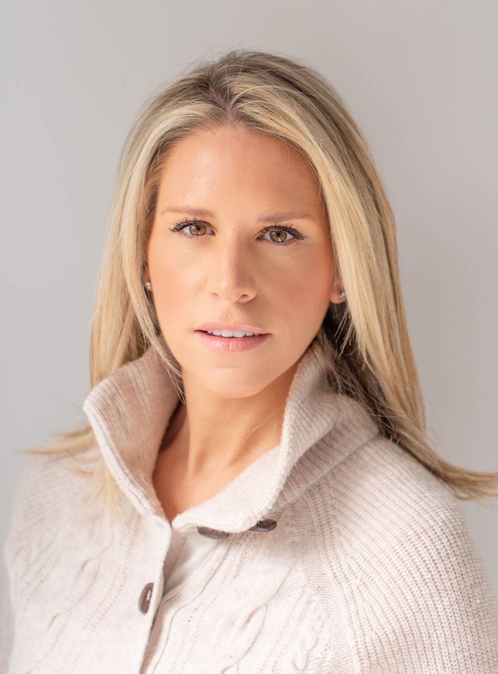 Professional portrait of a blonde woman wearing a cozy beige knit sweater with a fold-over collar.