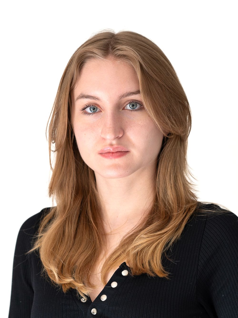 A headshot portrait in natural light against a white background showing light brown hair and a black button-up top.