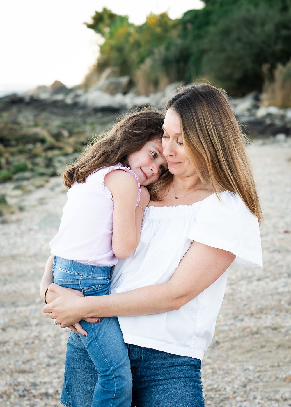 A tender moment shared between parent and child as they embrace on a rocky beach at sunset.