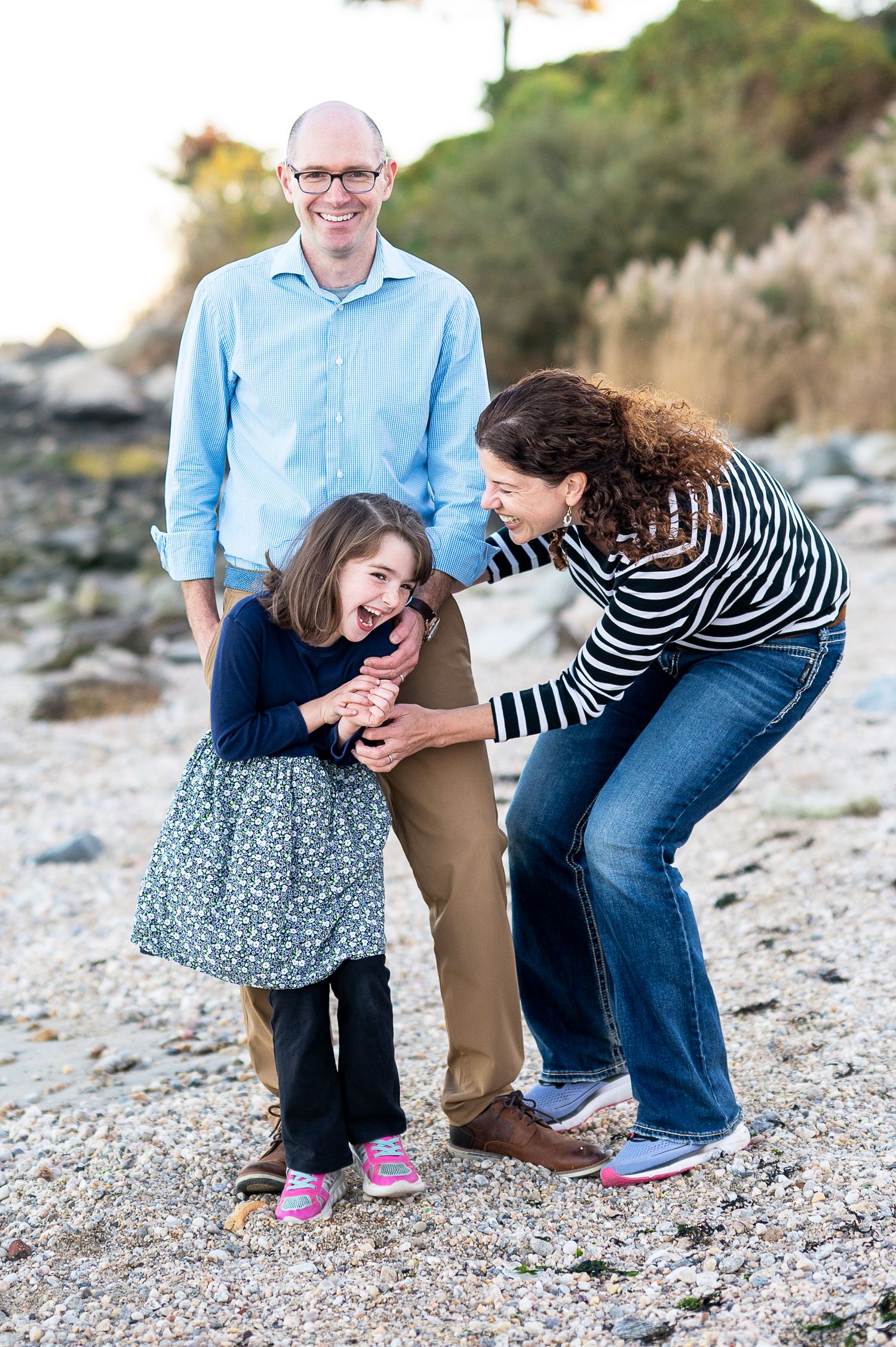 A candid family moment of shared laughter and joy together on a rocky beach at sunset.