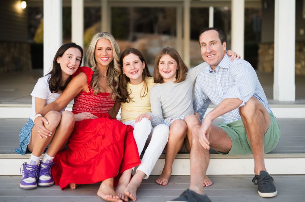 Family sitting casually together on white steps outdoors while smiling and laughing.
