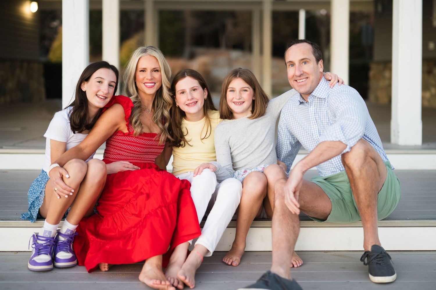 Family sitting casually together on white steps outdoors while smiling and laughing.