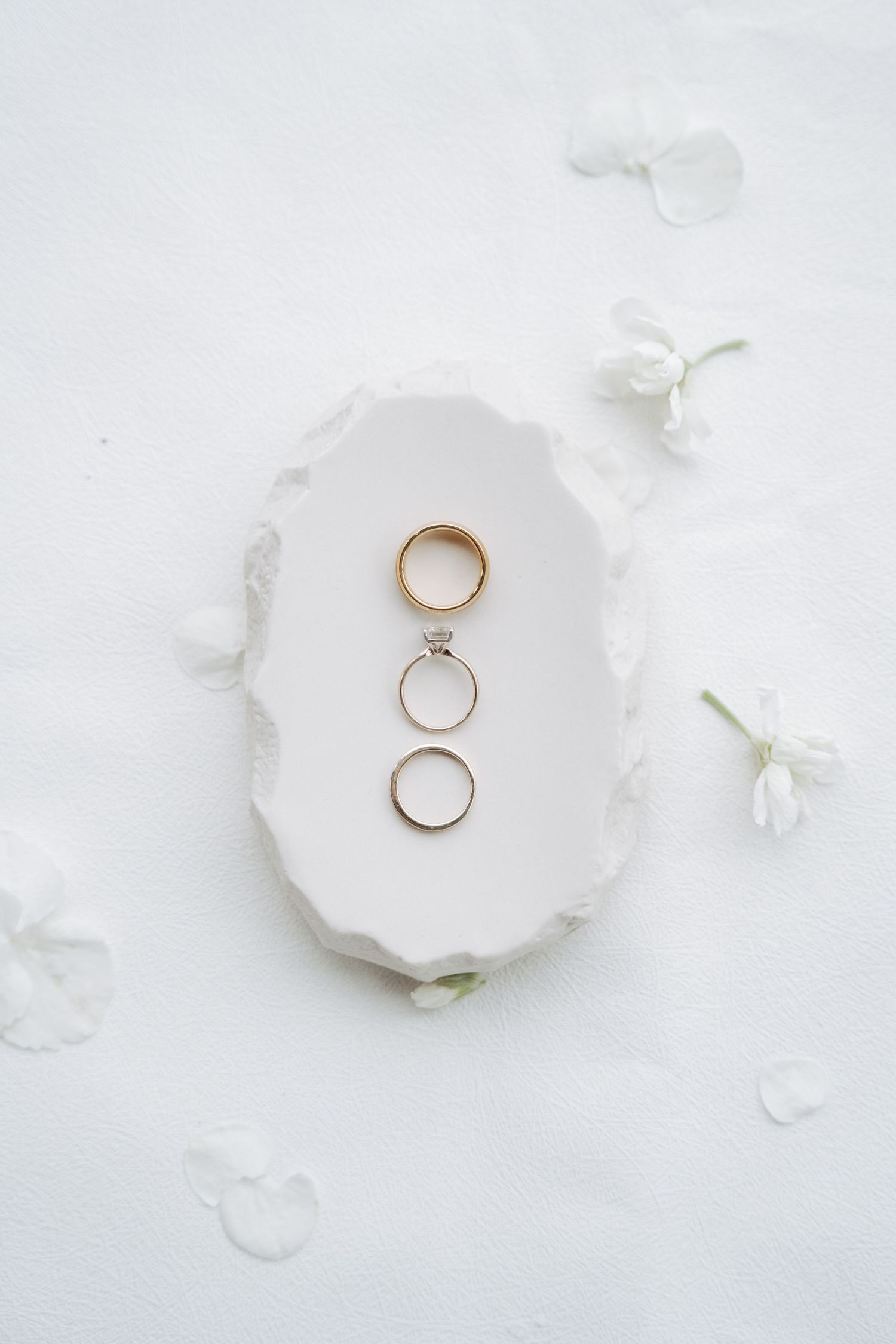 Wedding rings elegantly displayed on white ceramic plate with scattered petals.