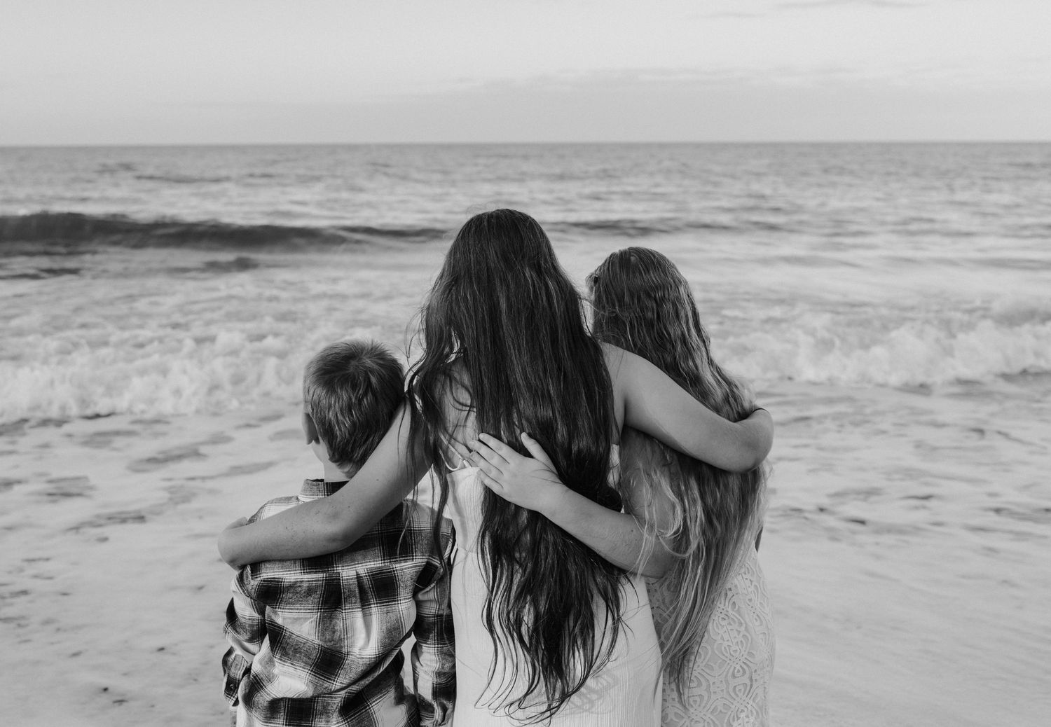 A family relaxes together on a couch in an intimate black and white photograph showing a tender moment at home.