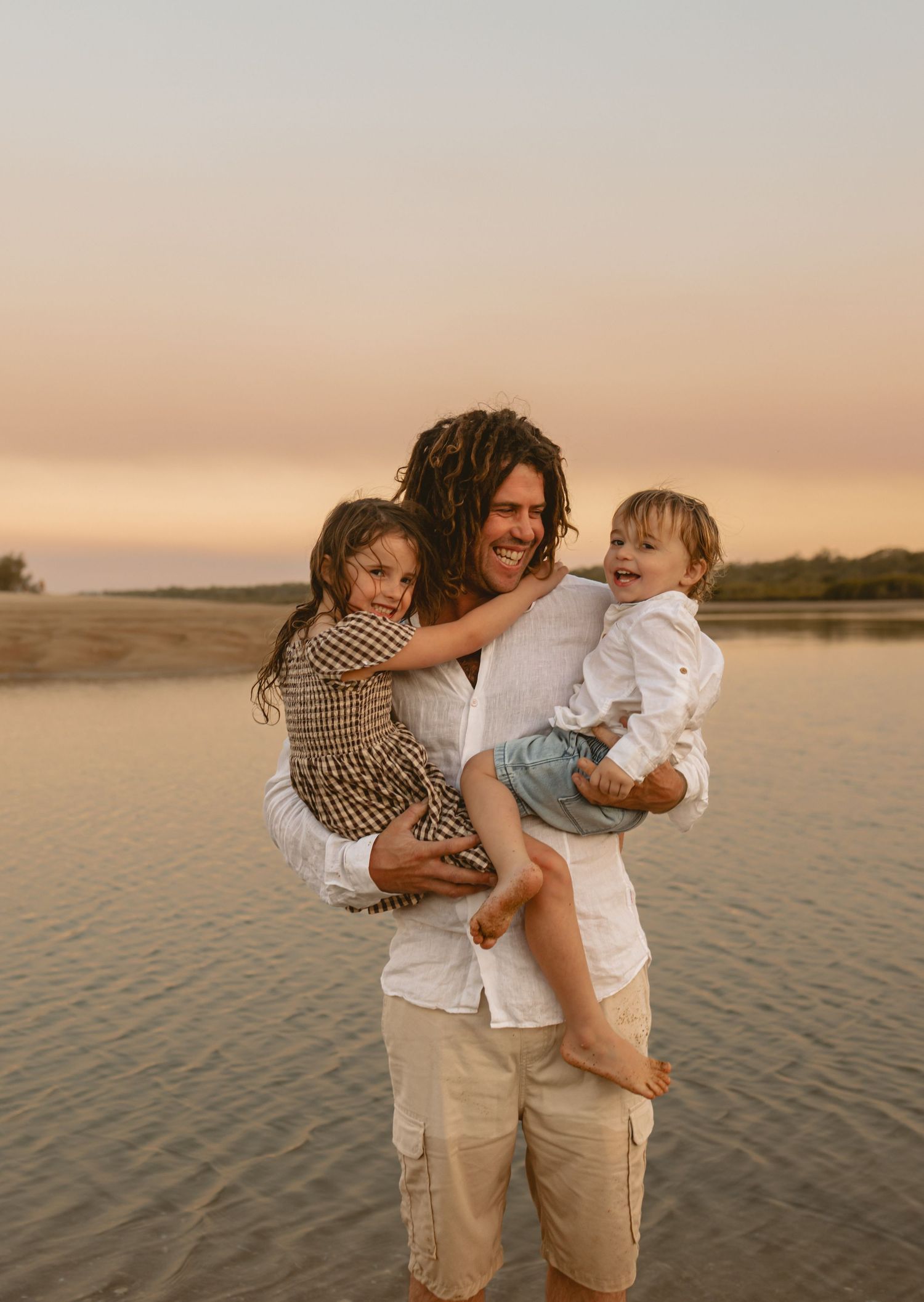 A family enjoys a tender moment together while standing on wet sand during golden hour at the beach.