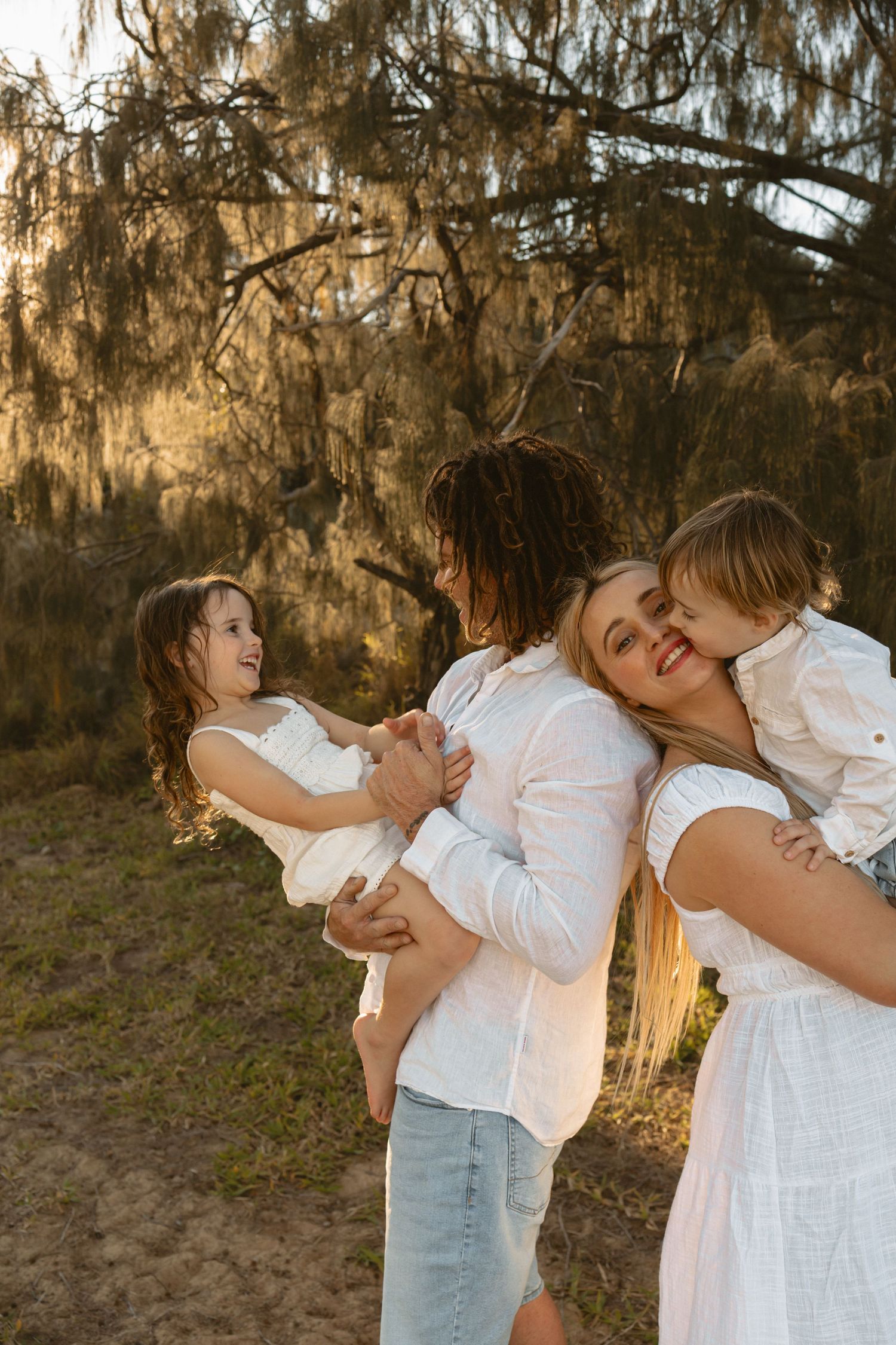 Parent and child in white outfits embrace lovingly during an outdoor photo session at golden hour.