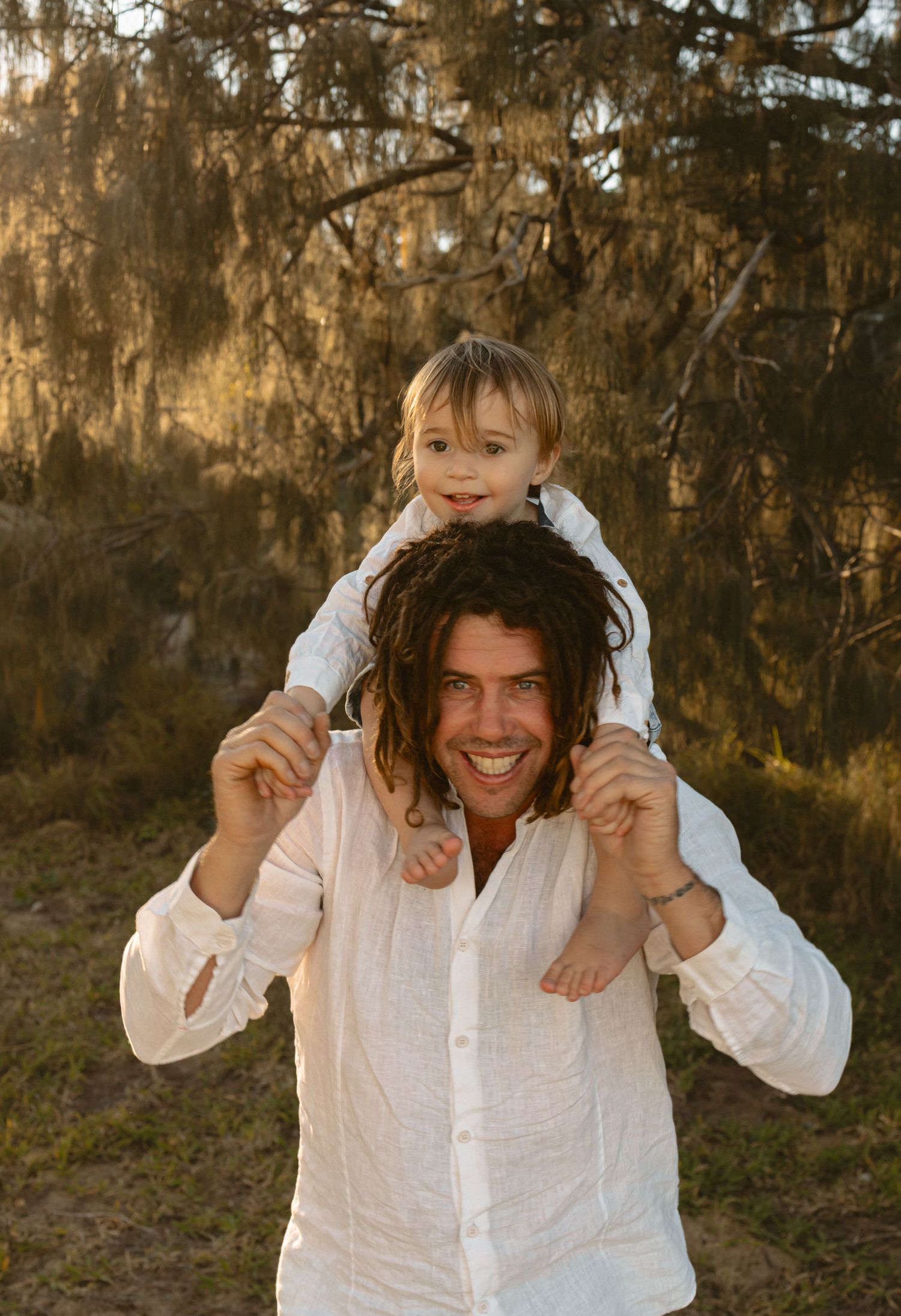 A playful family captures candid moments together in white outfits during a golden hour photoshoot in nature.