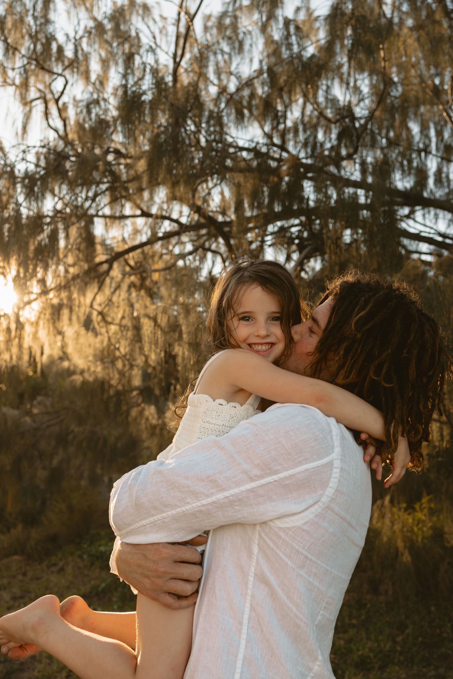 Romantic couple embraces in golden sunset light under Spanish moss draped trees.