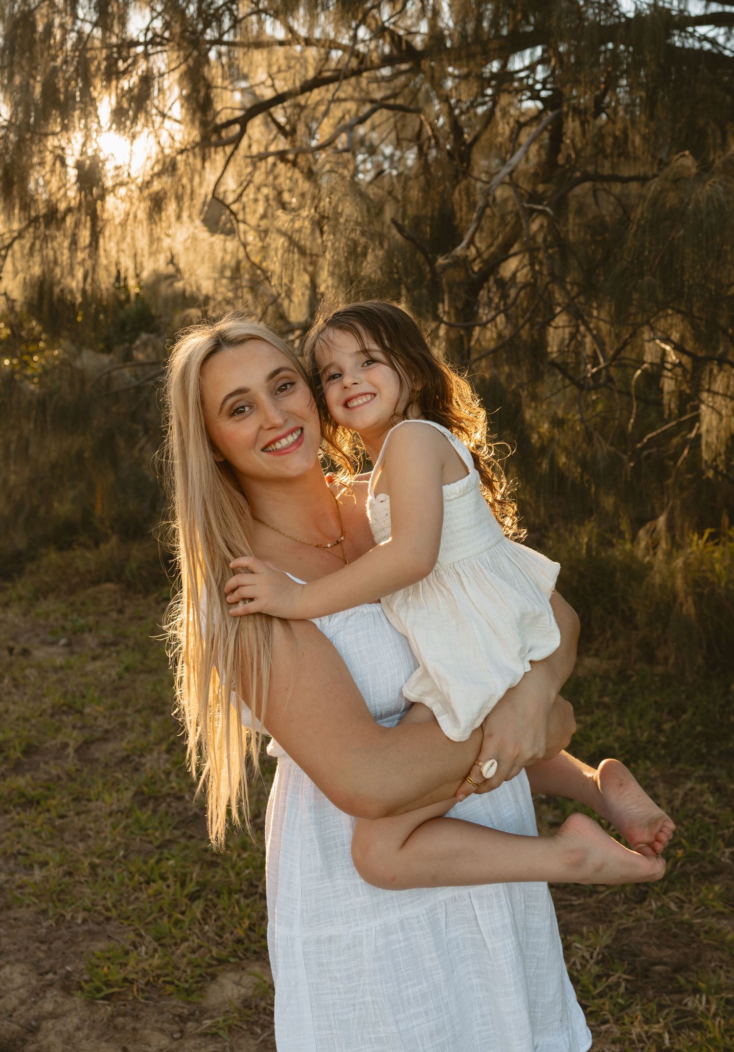 Golden afternoon sunlight filters through Spanish moss as two figures share affectionate embraces in a scenic outdoor setting.