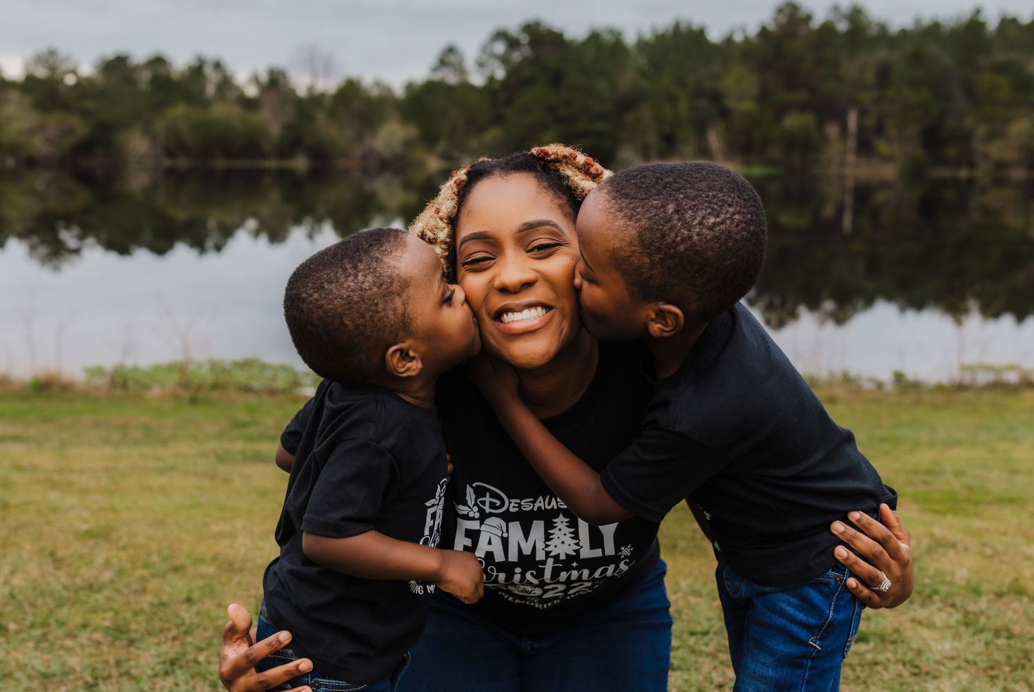 A warm family moment captured outdoors by a lake with loving embraces and joyful expressions.