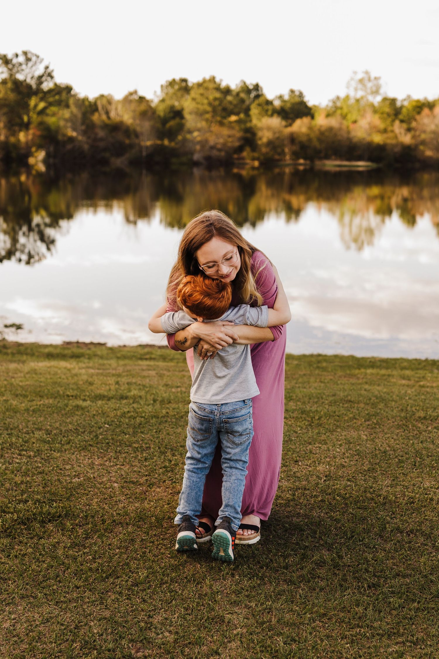 Caring embrace shared between two people on grassy lawn with reflective pond in background.