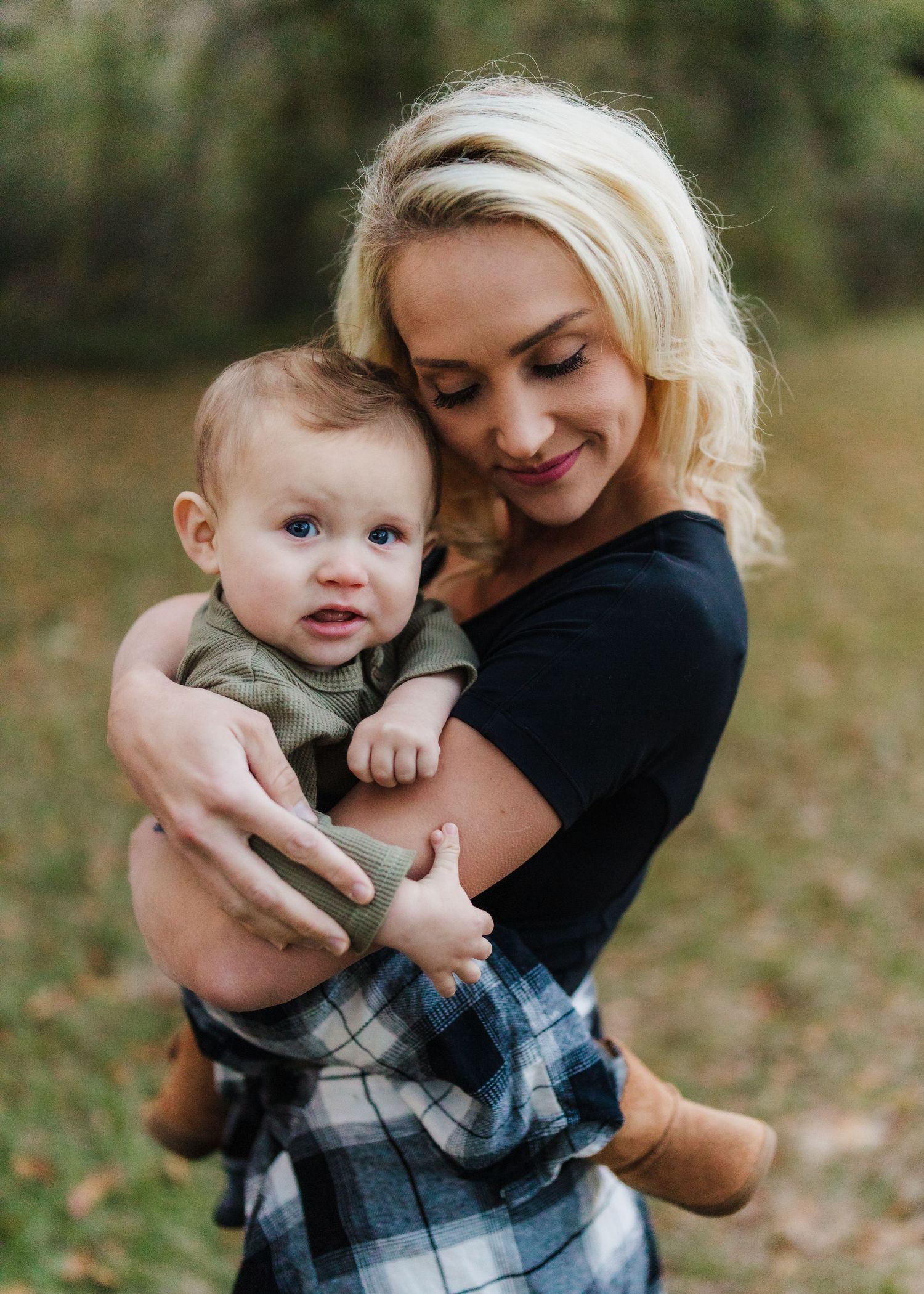 Tender moment captured between parent and baby against natural outdoor backdrop.