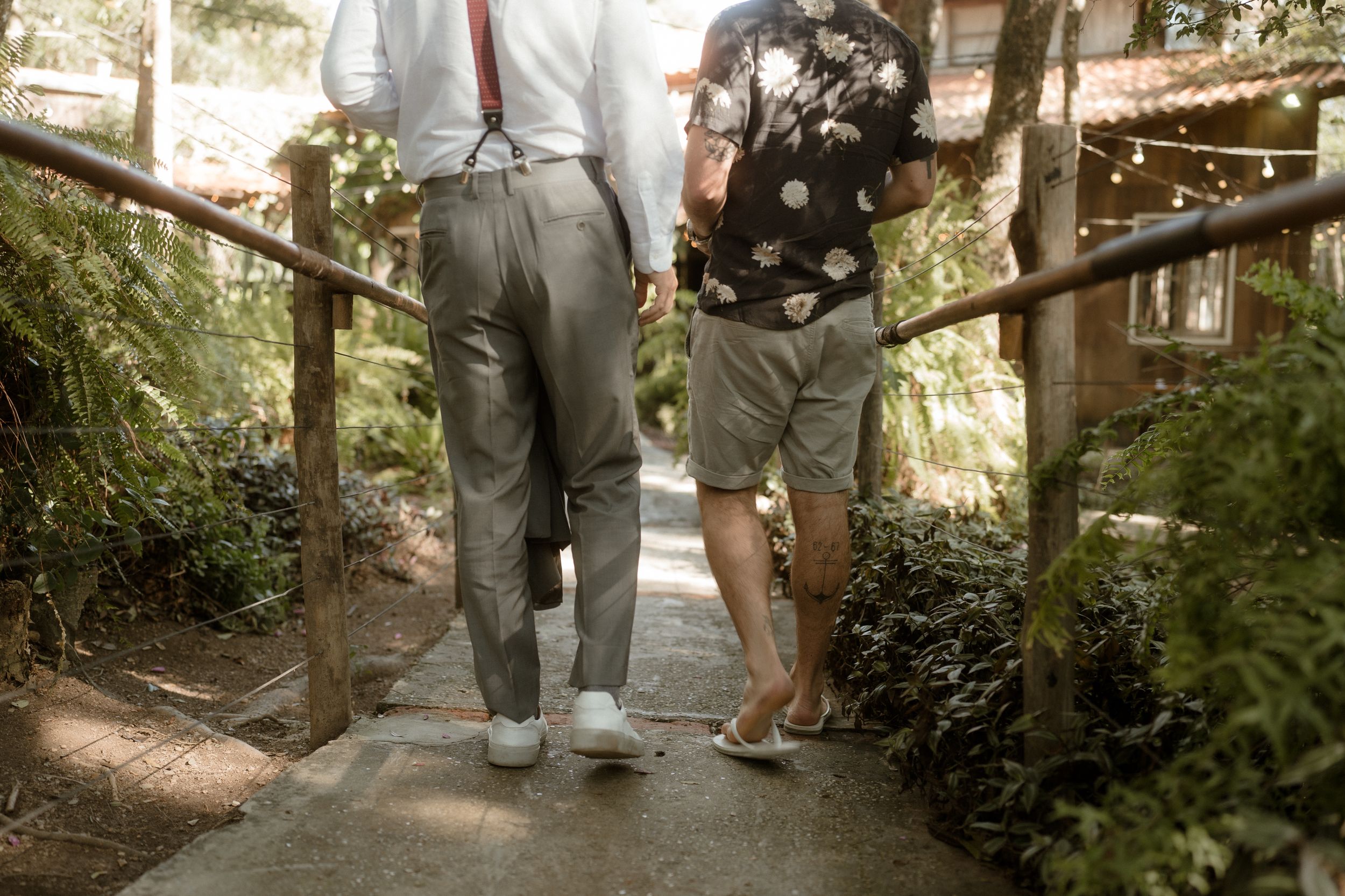 Two people walking together on a garden path wearing casual attire with one in shorts and one in pants.