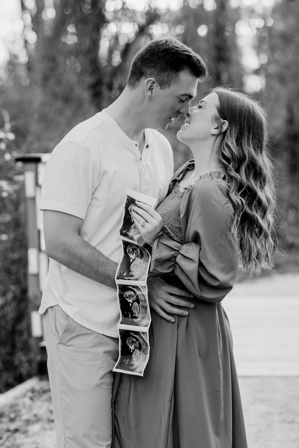 Black and white photo of a couple sharing a romantic moment while holding ultrasound photos.