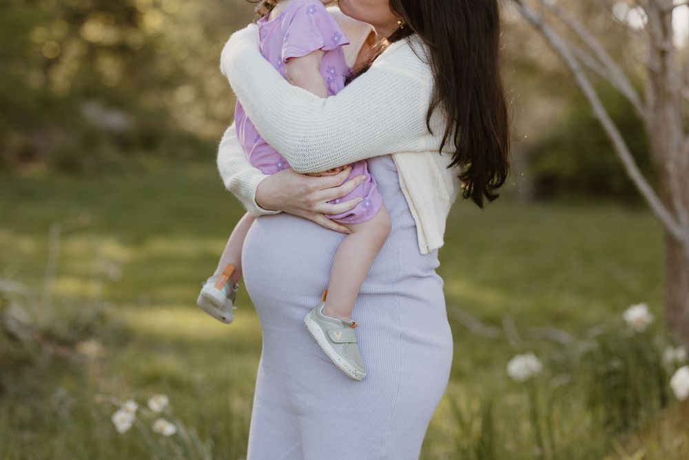 A mother wearing white holds a baby against a blurred garden background.