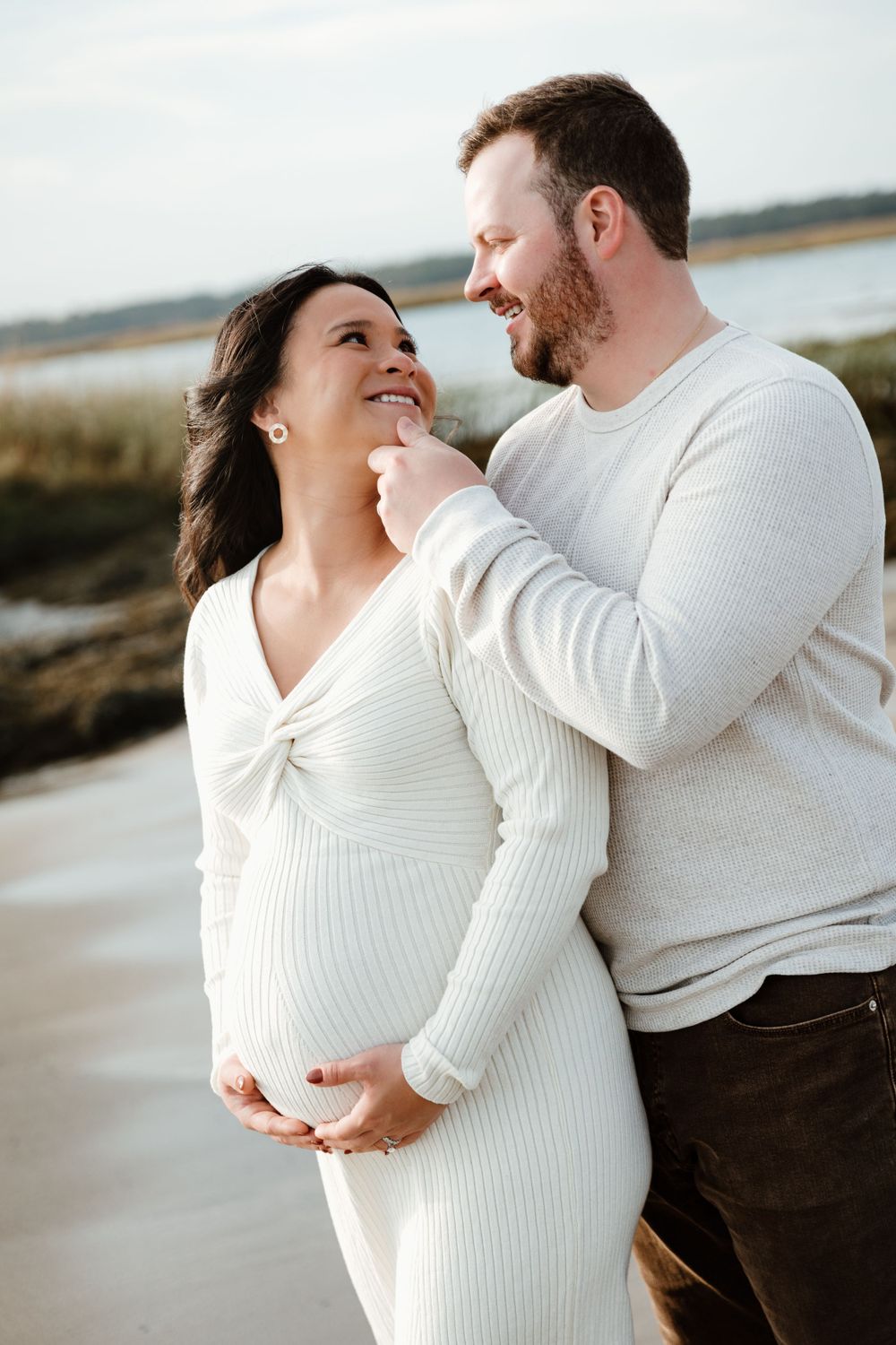 Intimate beach maternity portrait of couple in white sweaters.