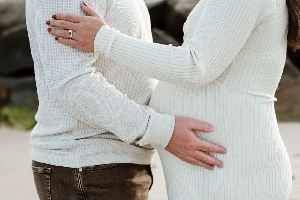 Close up of hands cradling pregnant belly in white knit dress.