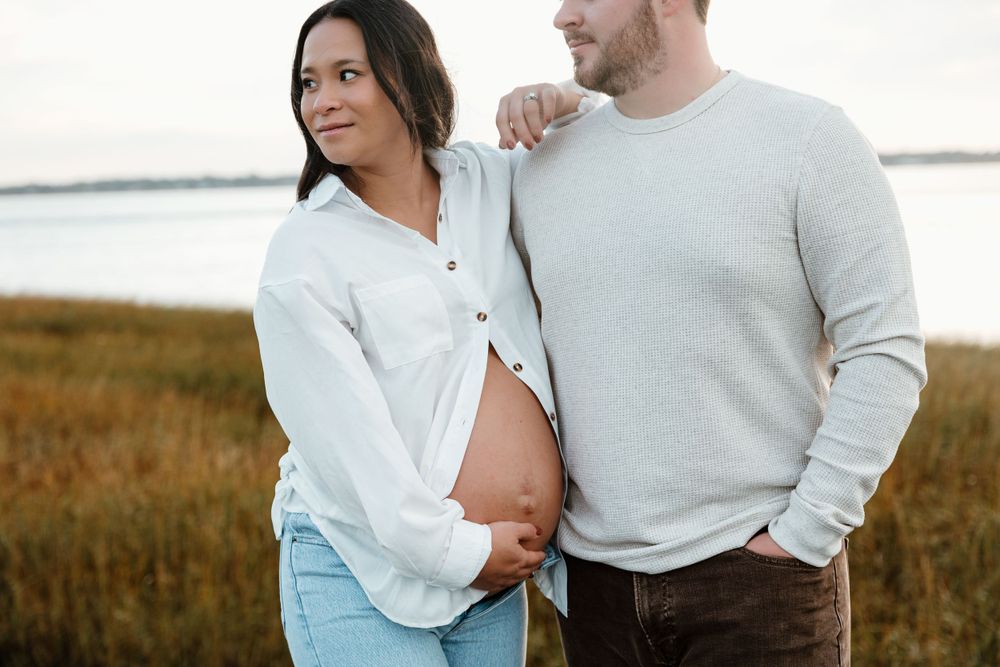 An expectant couple shares an intimate moment by the water during a maternity photoshoot.