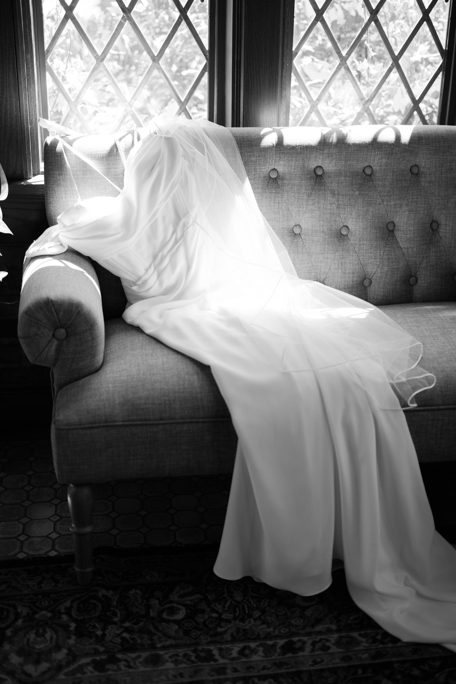 Wedding dress elegantly draped over a tufted gray couch near a window.