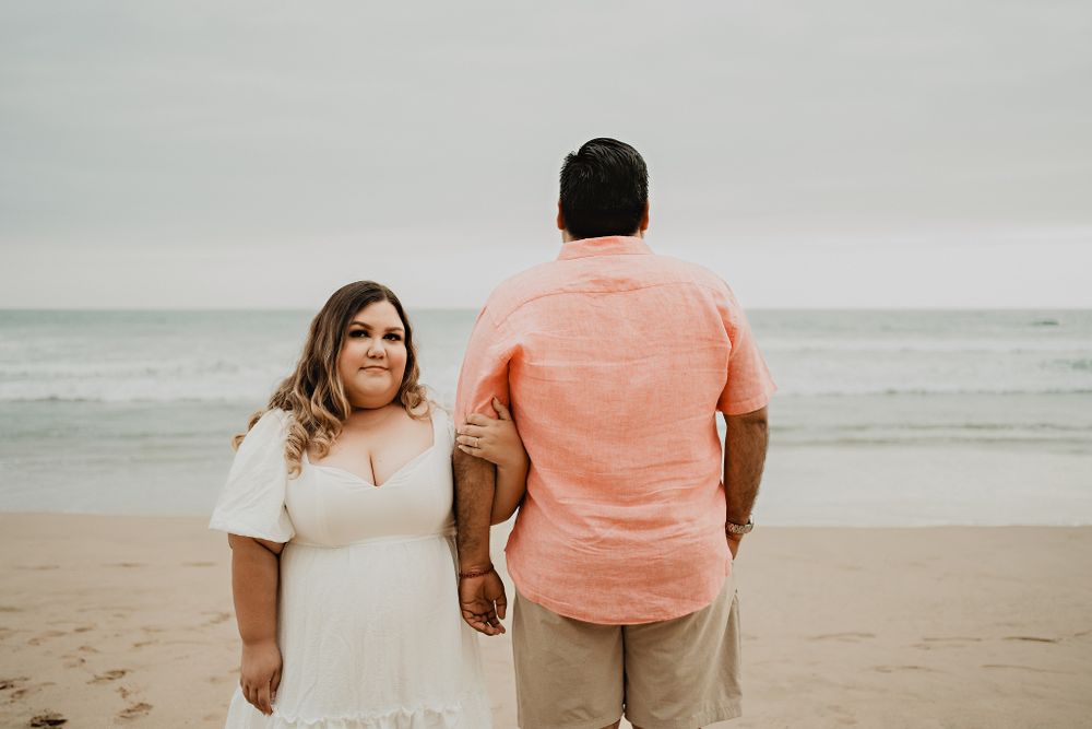 Groom facing away, bride smiling at camera, beach and ocean background