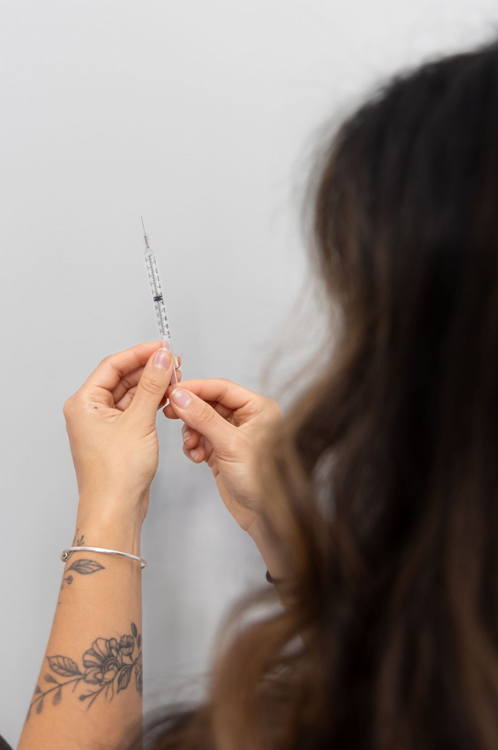 Close-up of female injector hands with floral tattoo carefully holding a syringe for cosmetic treatment.