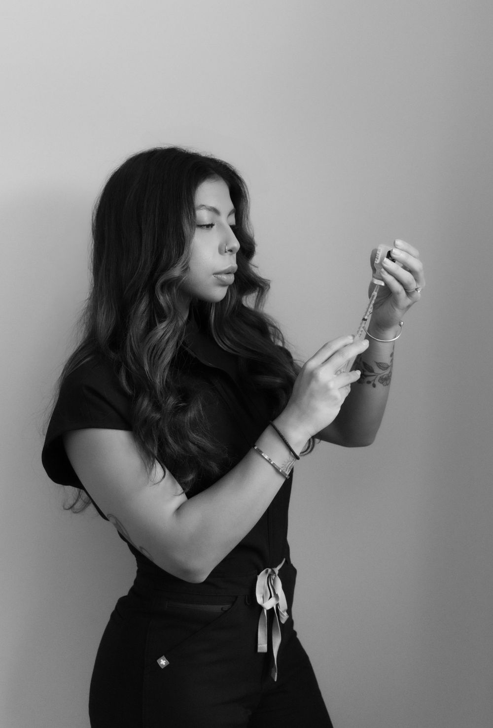 Black and white photo of a female nurse in scrubs carefully examining a syringe preparation.