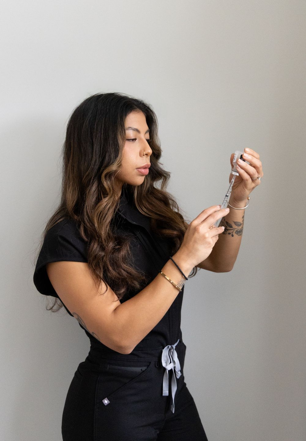 Female medical professional in black scrubs carefully preparing a syringe with injectable solution.