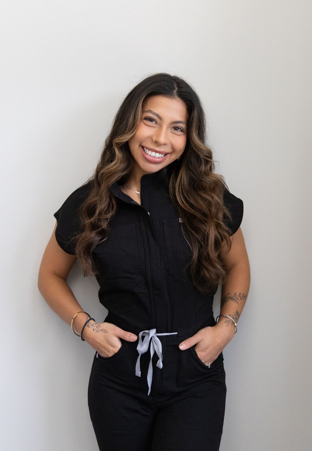 Smiling woman in black scrubs posing against a white wall.
