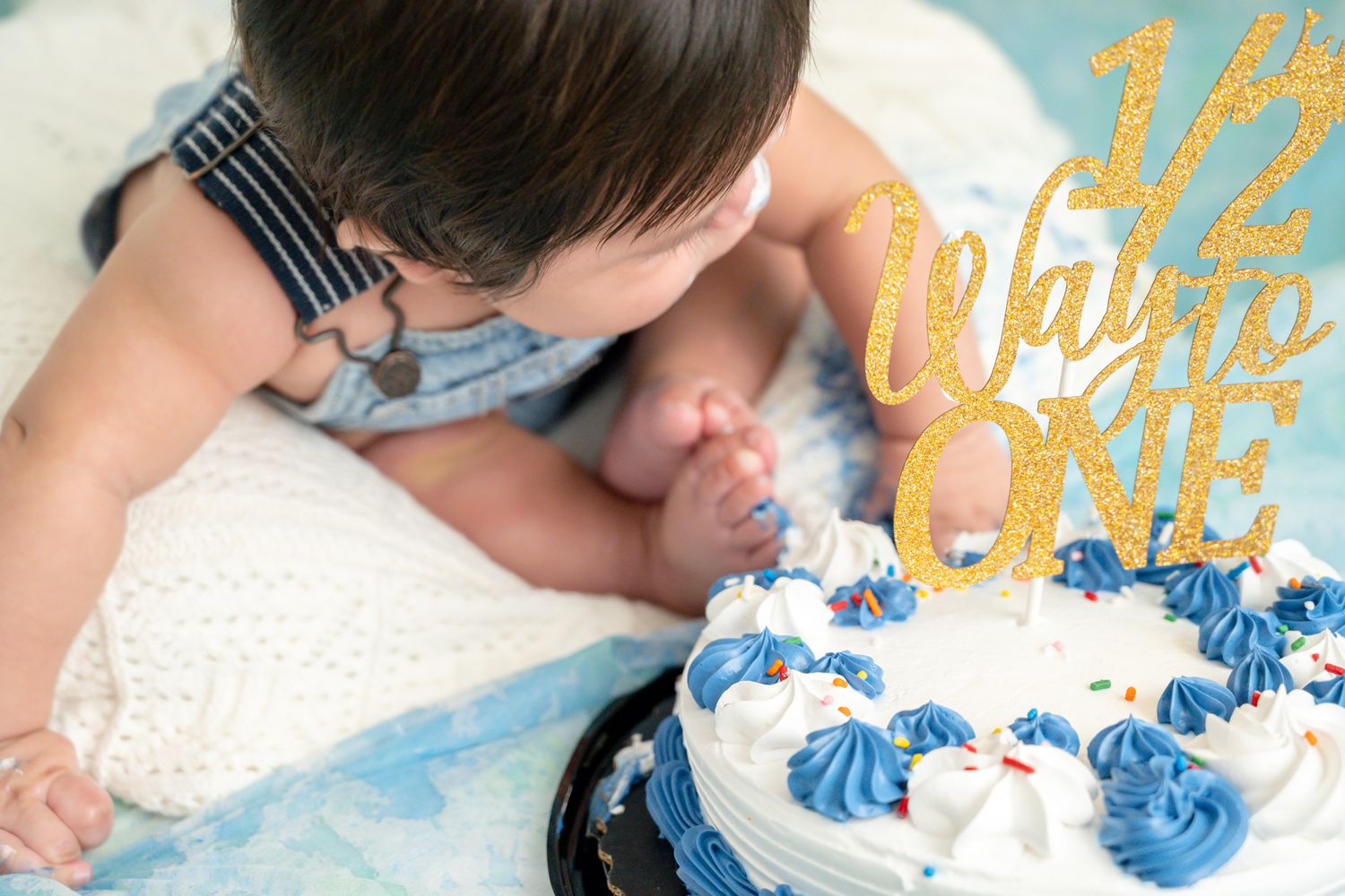 Child leaning over a birthday cake with blue frosting and gold decorations.