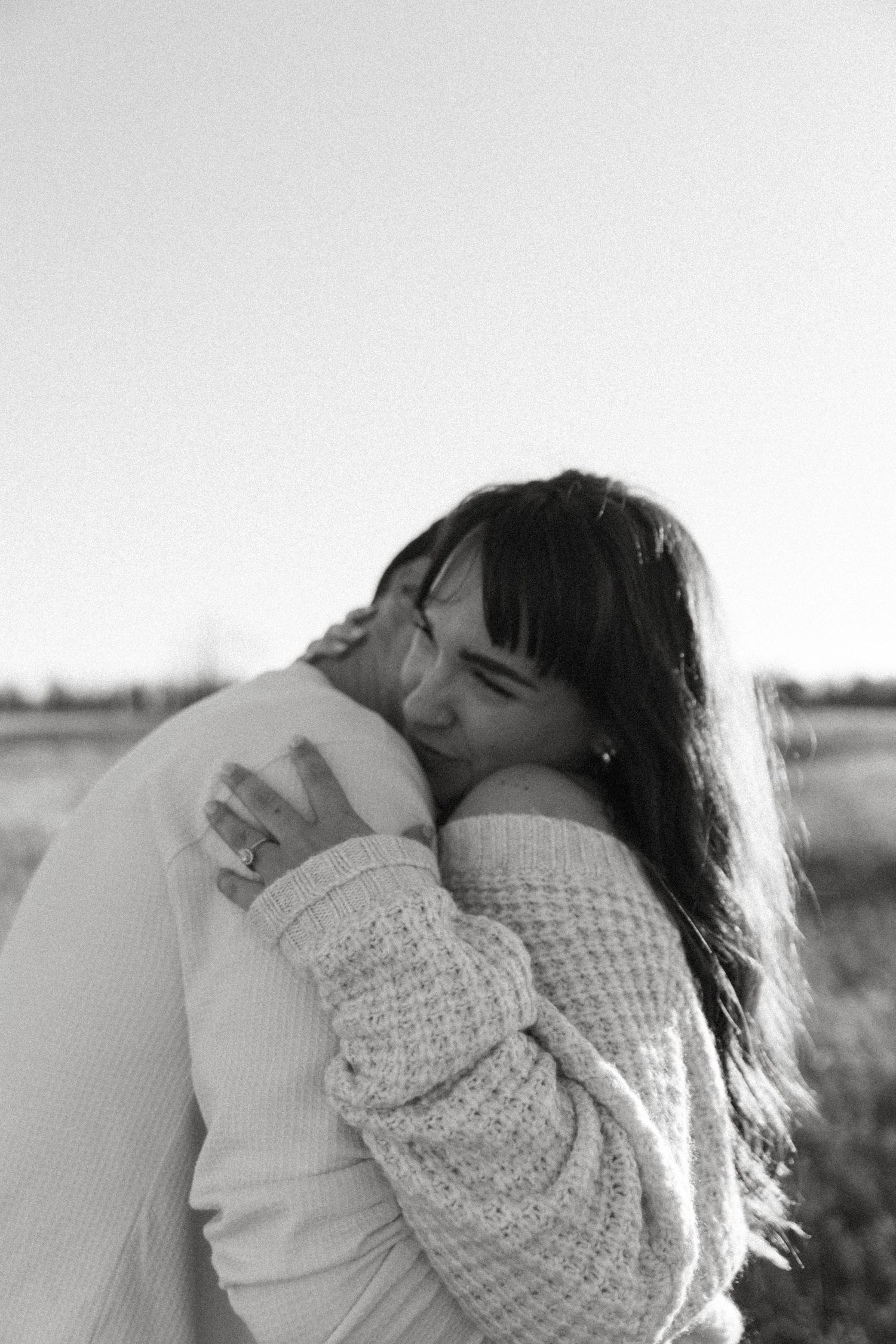Two people sharing an intimate embrace in a black and white candid moment outdoors.