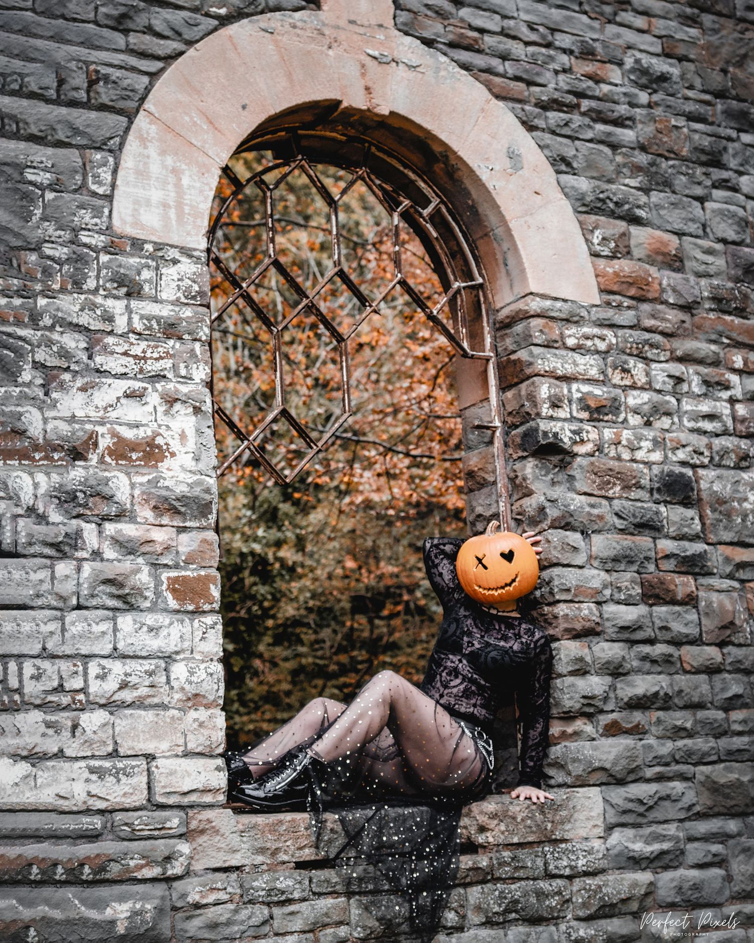 Halloween themed figure with jack-o-lantern head perched in gothic stone doorway.
