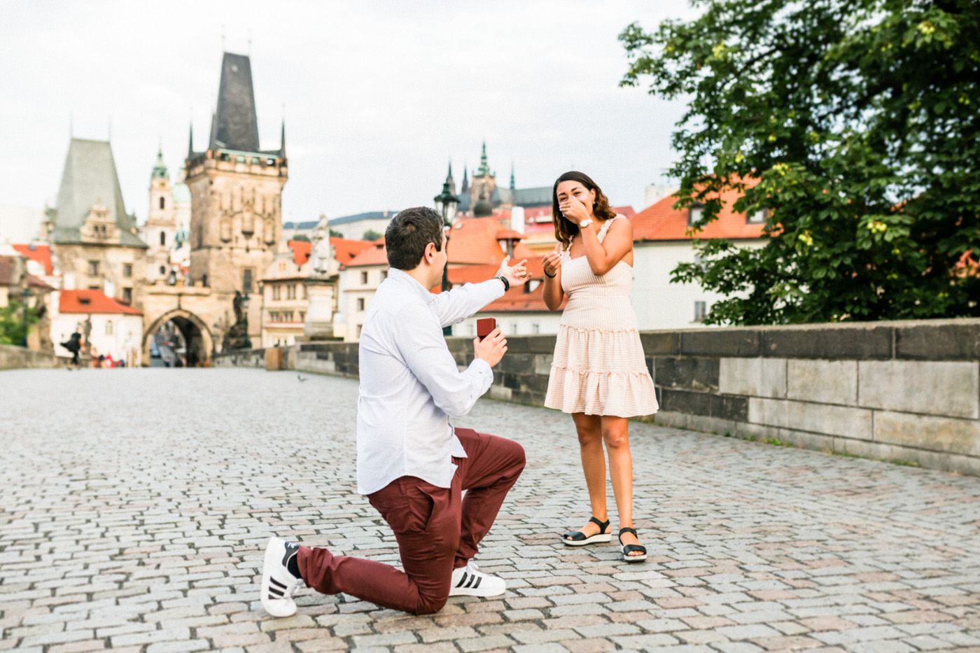 Marriage proposal on Charles Bridge in Prague with historic architecture in background.