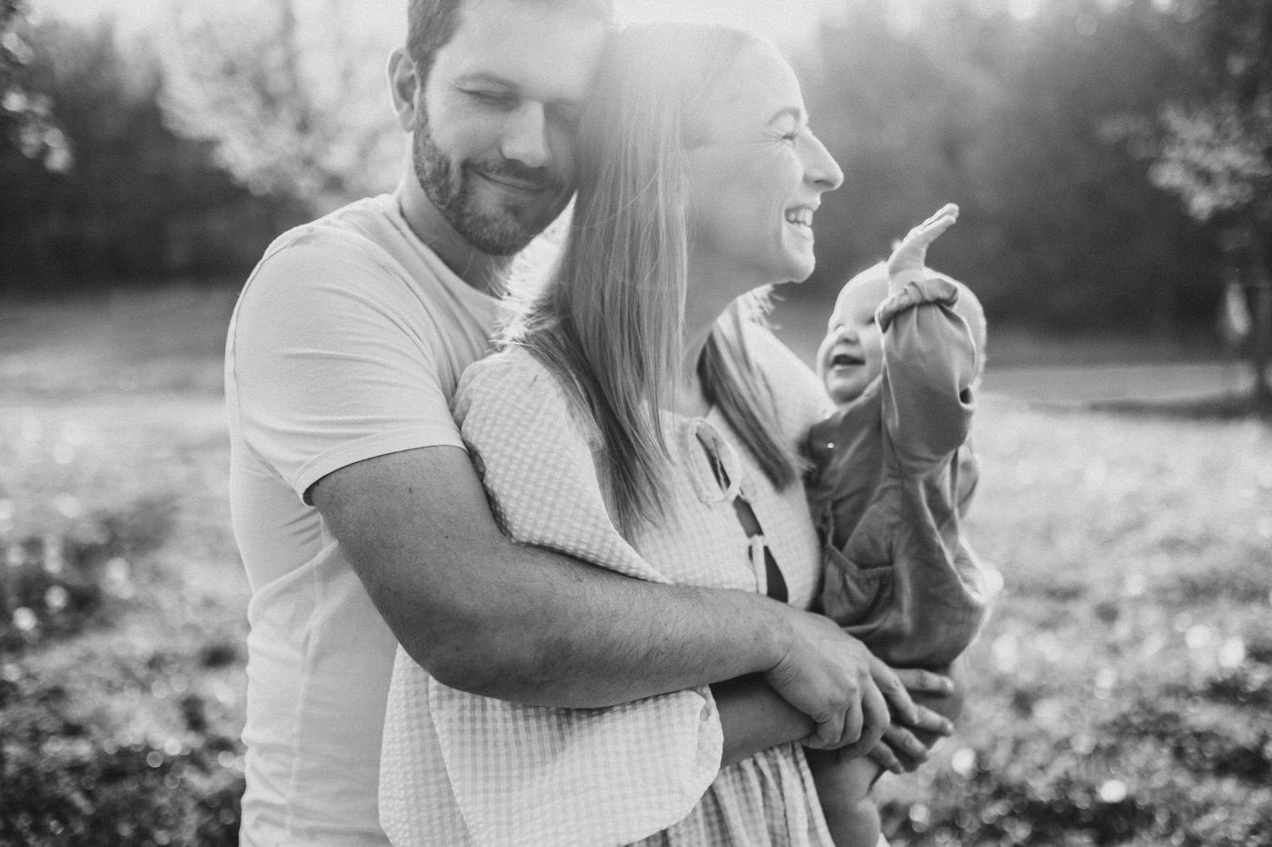 Black and white photo of couple embracing in sunlit meadow during summer evening.