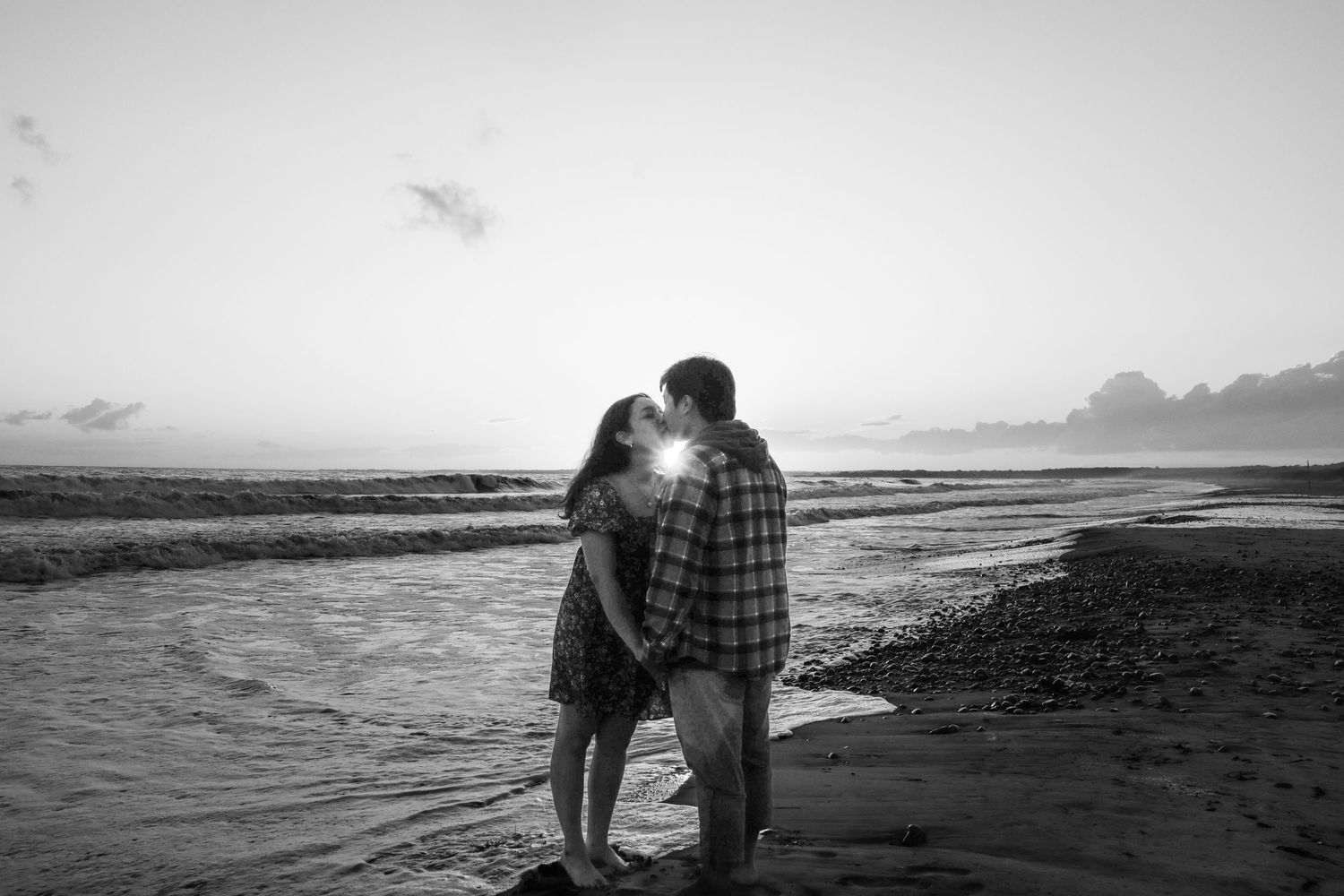 Couple embracing on beach at sunset creating romantic silhouette.