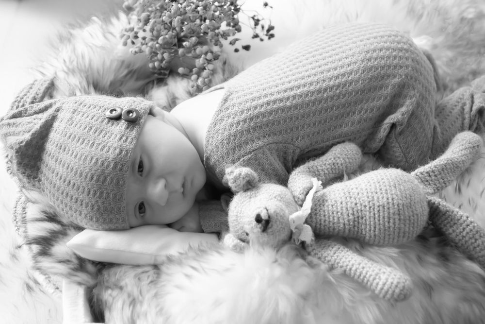 Black and white photo of someone lying down on soft fur with a small stuffed animal bunny toy beside them.