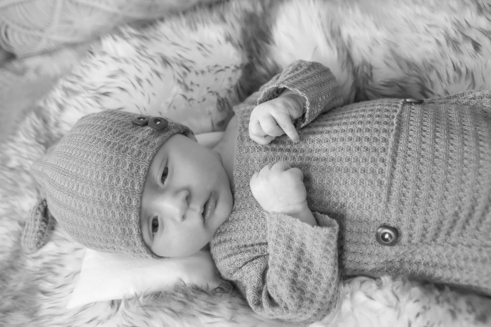 Black and white filmstrip showing a baby wearing a knitted cardigan laying on blankets in multiple poses.