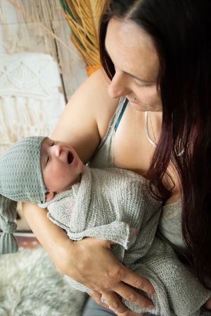 A tender moment between parent and newborn baby wearing a knit hat and wrapped in a cozy gray blanket.