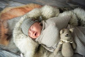 Newborn baby sleeping peacefully on fluffy fur blanket with knitted gray sweater and soft toy bunny.