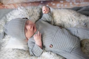 Newborn baby wearing cozy grey knitted sweater lying on soft white fur blanket.