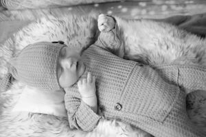 Monochrome photo showing a baby lying on textured white bedding with eyes closed peacefully.