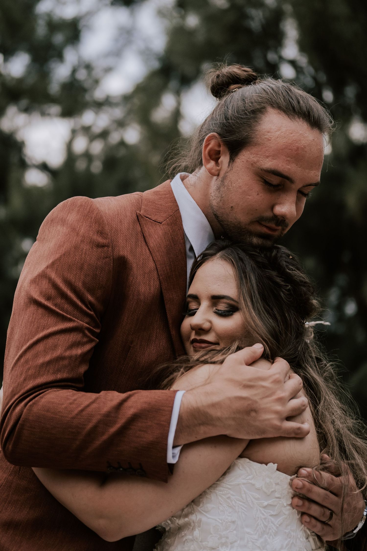 Intimate moment between couple in formal attire against moody forest backdrop.