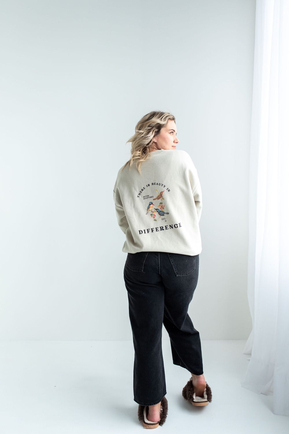 Person wearing a cream colored sweatshirt and black wide-leg pants poses against white background in casual style.