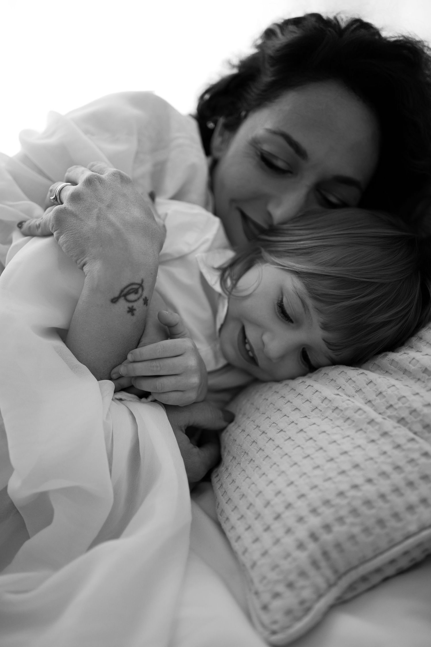 A black and white photo of a mother tenderly embracing her sleeping child on a pillow.
