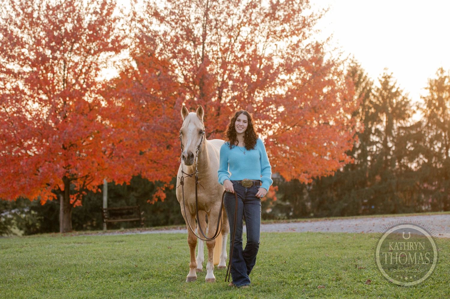 A person walks with a pale horse against vibrant orange fall foliage.