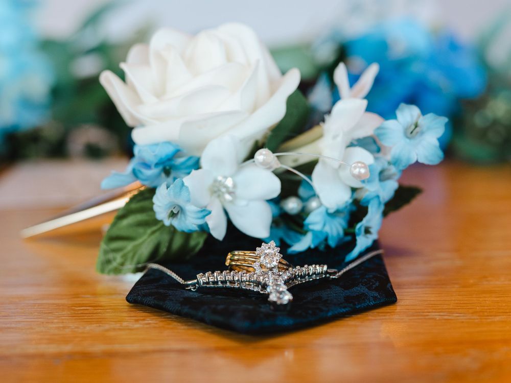 A white rose and light blue delphinium floral arrangement next to a sparkly tiara on black velvet.