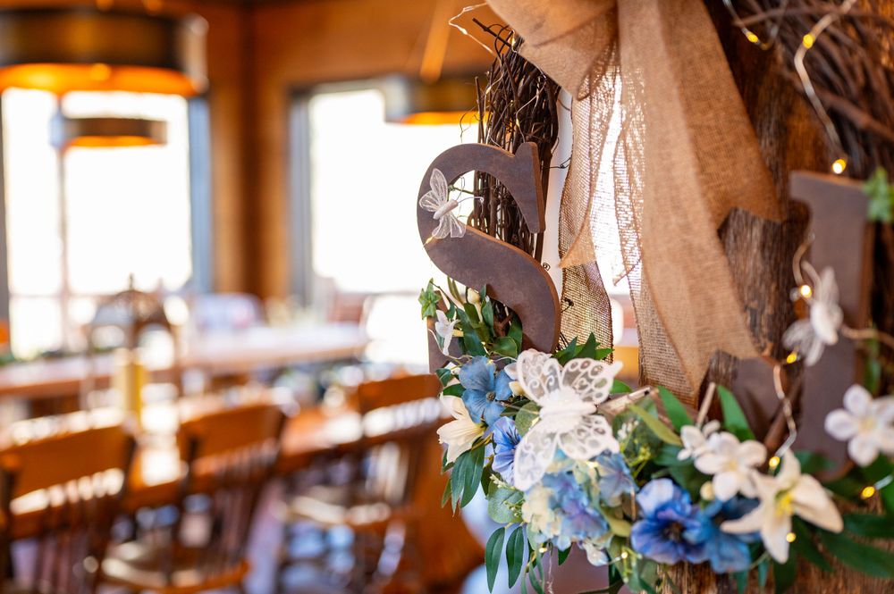 Rustic wedding decor features delicate blue and white flowers with greenery hanging against a burlap backdrop in a restaurant.