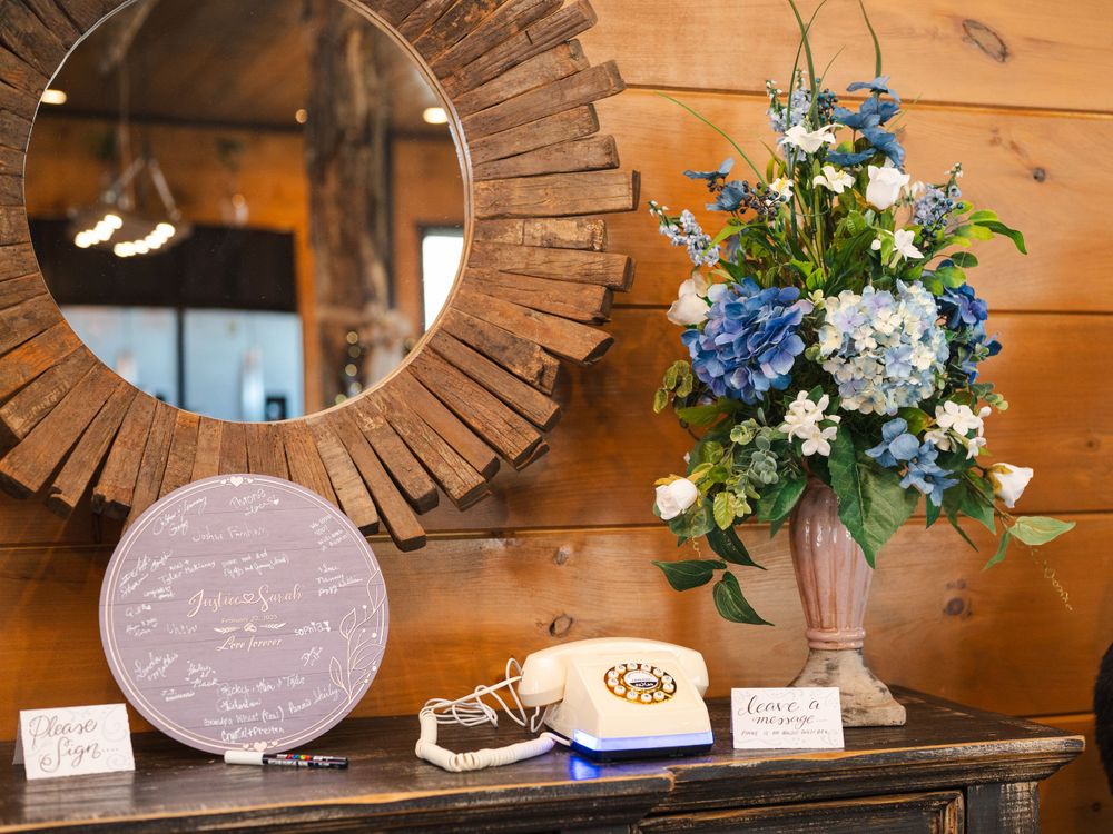 Rustic wooden wall decor with sunburst mirror, vintage rotary phone, and blue hydrangea floral arrangement on dark table.