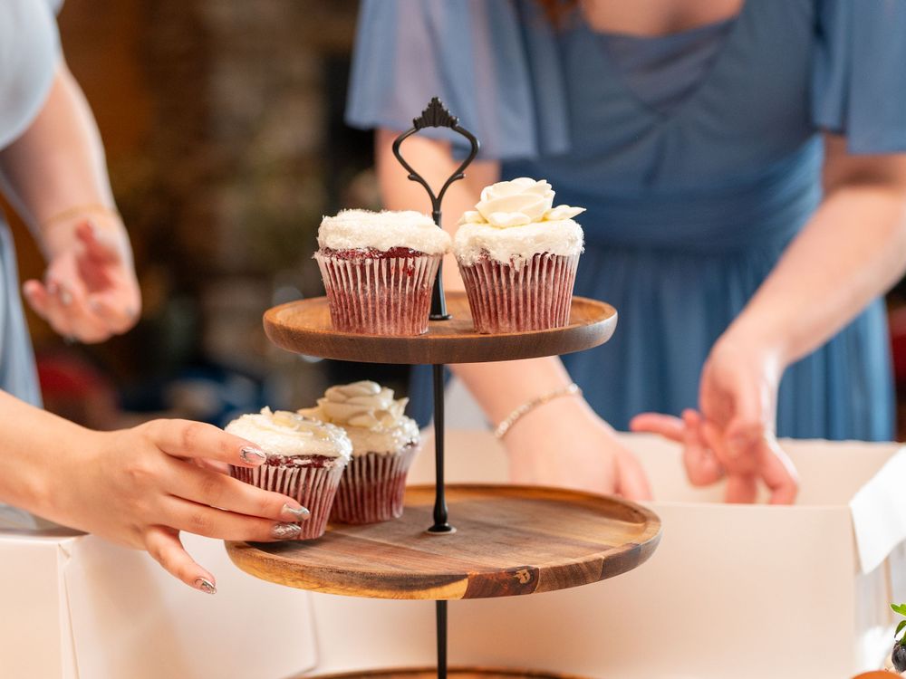 Two tiered wooden cake stand displaying chocolate cupcakes with white frosting on a white table.